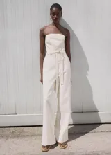 Mono largo color blanco de algodón estilo denim, con escote palabra de honor (strapless), pernera recta y un cinturón desmontable de la misma tela.