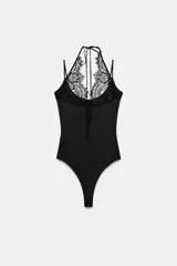 Body negro de tejido elástico con escote redondo y tirantes finos. Presenta un panel superior de encaje floral a tono con diseño halter ajustable mediante lazada en el cuello y cierre inferior con botones a presión.
