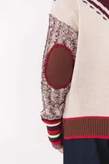 Cardigan de punto con diseño multicolor, cuello tipo polo con rayas, cierre frontal con botones y bolsillos aplicados. Presenta mangas con trama trenzada, coderas en contraste y bordado de la marca en el frente.