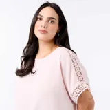 Camiseta rosada con cuello redondo y mangas cortas holgadas que presentan detalles de bordado y macramé.