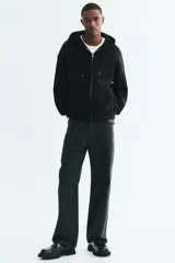 Campera canguro de felpa negra con capucha ajustable, cierre frontal completo y bolsillos tipo parche, de corte oversized.
