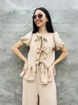 Blusa estampada con hojas verdes y blancas, con escote en V y mangas cortas abullonadas. Presenta volados en el ruedo y detalle de lazos en el frente.