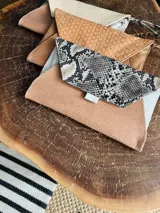 Sobre de cuero color naranja con estampado animal print, forrado y con bolsillo interior con cierre. Incluye pulsera desmontable.