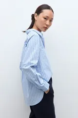 Camisa oversized de manga larga color celeste con rayas verticales finas en azul oscuro. Tiene cuello clásico y puños abotonados.