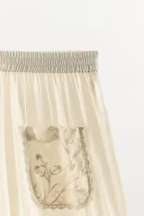 Pantalón de tiro alto con cintura elástica, confeccionado en viscosa. Presenta bolsillos de plastrón en el frente, aplicaciones de puntilla y bordados florales a tono, con bajo acabado en volantes.
