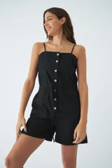 Monoprenda corta de color verde oliva, con tirantes finos ajustables, cierre frontal con botones y cintura elástica con cordón ajustable. Cuenta con bolsillos laterales.