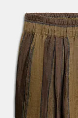 Pantalón ancho de lino 100%, color marrón y verde oliva, con rayas verticales. Presenta cintura elástica y bolsillos delanteros ocultos en la costura lateral.