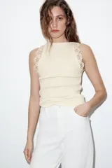 Top sin mangas de tejido rib color crema, con cuello redondo y detalle de encaje en los hombros.