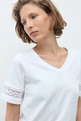 Remera blanca de algodón con cuello en V y mangas cortas que presentan un detalle de puntilla en los bordes.
