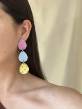 Aros colgantes con tres piezas en forma de gota de distintos colores: rosa con líneas celestes, celeste liso y amarillo con lunares naranjas.