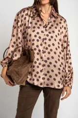 Camisa oversize de poliéster color rosa con estampado de lunares marrón oscuro, cuello camisero, cierre frontal de botones y mangas largas con puños elásticos.