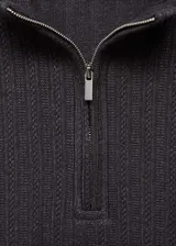 Buzo de punto acanalado en color gris oscuro, con cuello perkins y cierre frontal parcial con cremallera. Presenta un diseño entallado de manga larga.