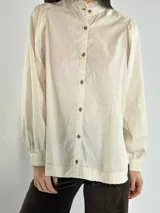 Camisa color beige con cuello mao, mangas largas abullonadas y cierre frontal con botones.