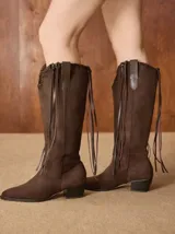 Botas de caña alta confeccionadas en gamuza color marrón, con diseño de flecos laterales y taco cuadrado de altura media.