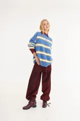 Sweater de textura peluda con diseño de rayas horizontales en tonos bordó, amarillo y azul. Presenta un corte holgado, cuello redondo y un pequeño logo bordado en el centro del pecho.