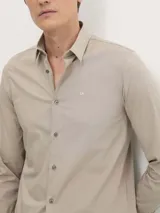 Camisa de vestir color beige claro, corte slim, de popelín de algodón elástico, con cierre frontal de botones y logo CK bordado en el pecho.