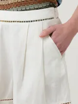 Short de lino orgánico color beige, de tiro medio y calce holgado, con detalles de aberturas bordadas en la cintura y en los dobladillos. Cuenta con bolsillos laterales y pinzas frontales.