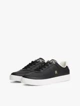 Zapatillas de corte bajo estilo tenis, confeccionadas en piel color negro. Presentan suela de goma blanca, detalle metalizado en el talón, ojal superior dorado y monograma TH metálico en el lateral.