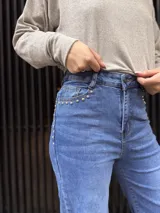 Pantalón de jean azul de corte recto y tiro alto, con detalle de tachas metálicas en los bolsillos delanteros y cierre frontal con botón.