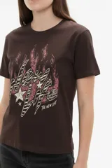 Remera de algodón negra de manga corta y cuello redondo, con estampa frontal que incluye letras rojas y gráficos en tonos dorados.