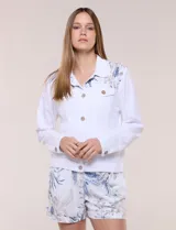 Campera liviana de lino color blanco, con estilo denim y silueta semi entallada. Presenta un canesú superior estampado con motivos florales en tonos azules y tostados, cuello camisero, abotonadura frontal con botones rústicos y bolsillos con solapa en el pecho.