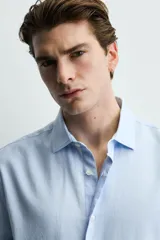 Camisa de corte regular fit confeccionada en tejido de algodón con textura twill. Presenta cuello italiano, manga larga con puños abotonados y cierre frontal de botones.