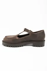Zapato tipo guillermina de cuero lavado color marrón, con diseño de tira en T y cierre de hebilla metálica. Presenta costuras decorativas en contraste y suela de goma con plataforma dentada.