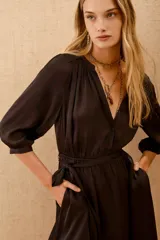 Vestido corto de color negro, con mangas tres cuartos, cuello mao y cierre frontal con botones. Incluye un lazo a tono para ajustar en la cintura y bolsillos laterales.