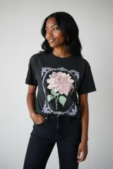 Remera de algodón color marrón con cuello redondo y mangas cortas. Presenta un estampado frontal con ilustraciones de dos copas de cóctel decoradas con lazos.