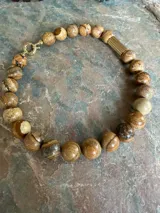 Collar de piedras naturales en tonos tierra, con detalle de tubo dorado en un lateral y cierre marinero dorado.