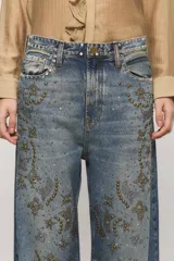 Jeans de tiro medio y calce holgado, color azul con lavado desgastado. Presenta tachas metálicas aplicadas en la parte frontal formando patrones decorativos y en la pretina.