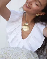 Collar artesanal con dije central de metal con textura orgánica irregular que evoca una ostra. El dije está montado sobre un cordón de algodón natural, permitiendo un uso versátil y regulable.