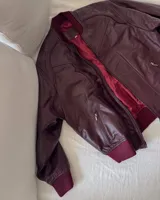 Campera tipo bomber de cuero ovino color marrón oscuro, con cuello de tejido acanalado y cierre frontal con cremallera.
