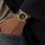 Reloj analógico Guess con caja de acero inoxidable en tono dorado y esfera negra con números romanos. Cuenta con una malla de silicona negra y movimiento de cuarzo.