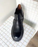 Botineta de cuero vacuno color negro con suela track de goma. Presenta una combinación de texturas en el cuero, incluyendo paneles con efecto croco en el talón y en la tira decorativa sobre el empeine, además de paneles laterales elásticos.