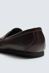 Mocasín de vestir en piel color marrón oscuro, con detalle de antifaz en el empeine, horma redonda y suela de goma Vibram.
