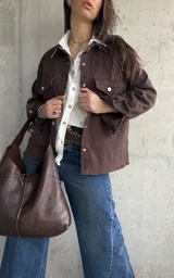 Sobrecamisa de gabardina color marrón chocolate, de corte holgado, con bolsillos con solapa en el pecho, mangas largas y cierre frontal de botones metálicos.