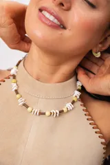 Collar corto de diseño artesanal con cuentas redondas amarillas, escallas blancas de caracol, cuentas tubulares marrones y pequeñas cuentas doradas.