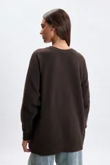 Buzo deportivo de corte oversize en color marrón, con cuello redondo y mangas largas tipo raglán. Presenta una estampa frontal con la inscripción 'Health Club' en tipografía cursiva y detalles de texto en blanco.