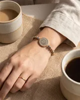 Pulsera de acero con baño de oro, compuesta por esferas metálicas en tonos dorados y plateados, con un dije central redondo decorado con cristales multicolor.