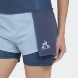 Short deportivo de tenis Le Coq Sportif, modelo Tennis Classic, de color azul oscuro con un short interior de compresión en tono celeste más claro. Presenta un diseño de doble capa y el logo del gallo en el lateral de la pierna derecha.