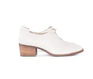 Zapato cerrado tipo mocasín con taco cuadrado de madera, confeccionado en cuero con textura de reptil en color crema. Presenta un detalle de hebilla metálica dorada en el empeine.