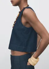 Top sin mangas de efecto denim con cuello redondo y diseño ajustado en la cintura con ligero vuelo en el bajo. Cuenta con cierre de botón en la parte posterior del cuello.