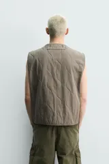 Chaleco acolchado de algodón color verde militar, de corte relaxed fit, con cuello en V, cierre frontal con cremallera y bolsillos de parche en la cadera. Presenta diseño acolchado con pespuntes ondulados y efecto lavado.