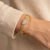 Pulsera de plata 925 con baño de oro, compuesta por una banda de malla metálica y una doble cadena fina colgante. Presenta un dije central en forma de corazón pavé con circonias.