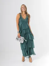 Vestido largo negro de seda italiana con diseño sin mangas de bretel ancho y escote en V profundo con detalles de paillettes plateados. Presenta múltiples capas con volados y bordes deshilachados que aportan movimiento y una caída fluida.