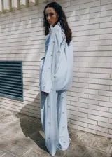 Camisa de popelina celeste a rayas, de corte oversize, con cuello camisero, mangas largas y aplicaciones de pedrería y lentejuelas brillantes distribuidas por toda la prenda.