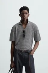 Polo de punto de manga corta con cuello solapa y abertura frontal en forma de V. Presenta un patrón de rayas horizontales finas en blanco y negro, con un acabado texturizado y un calce relajado.