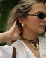 Collar con dije de forma irregular en tonos dorados y plateados, suspendido de un cordón doble de algodón negro.