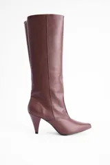 Bota de caña alta confeccionada en cuero vegano color marrón, con diseño de punta fina y taco aguja de altura media.
